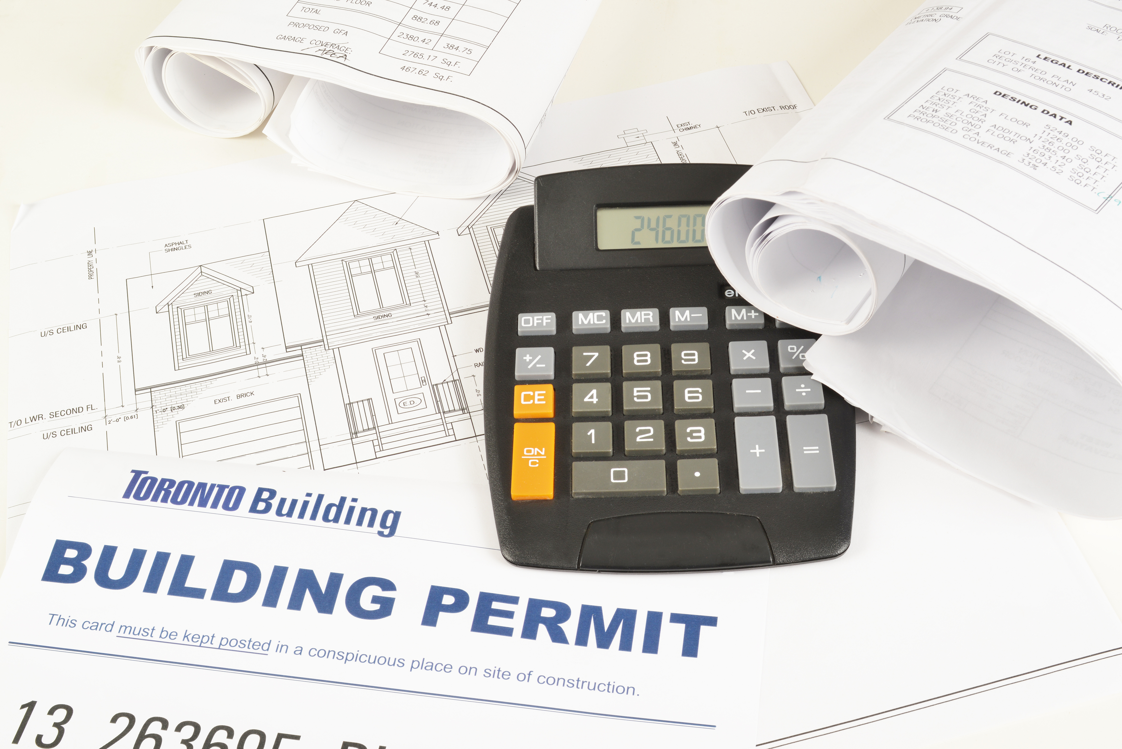 A calculator resting on building permit paperwork and architectural elevation drawings