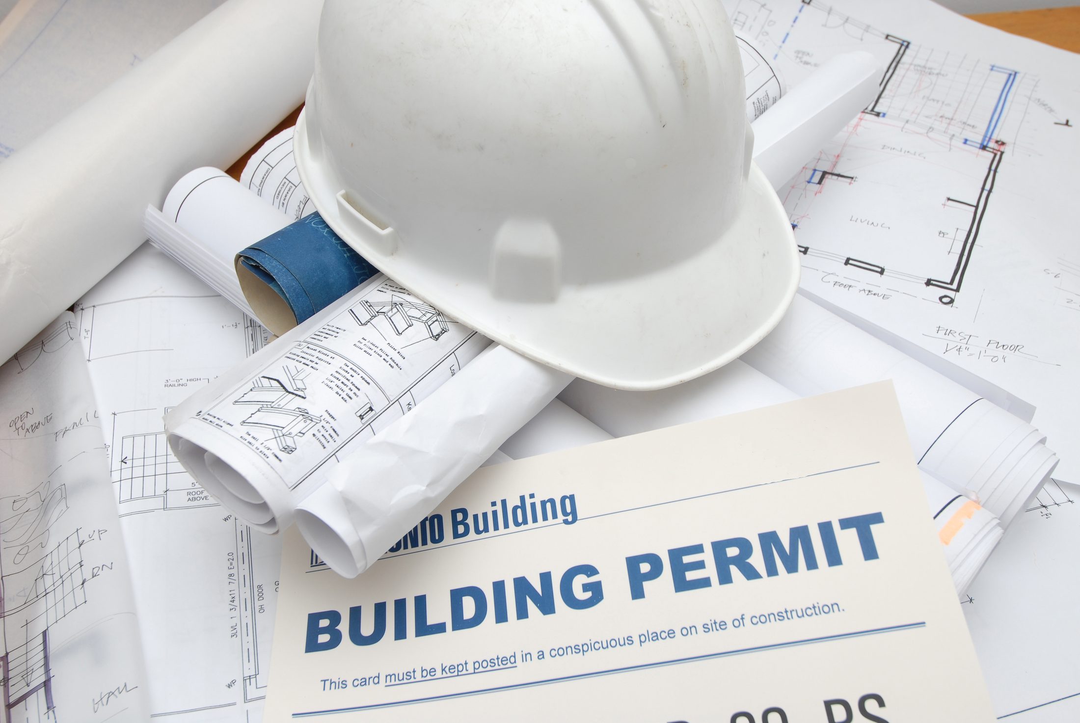 A white hard hat resting on rolled architectural drawings beside a building permit card